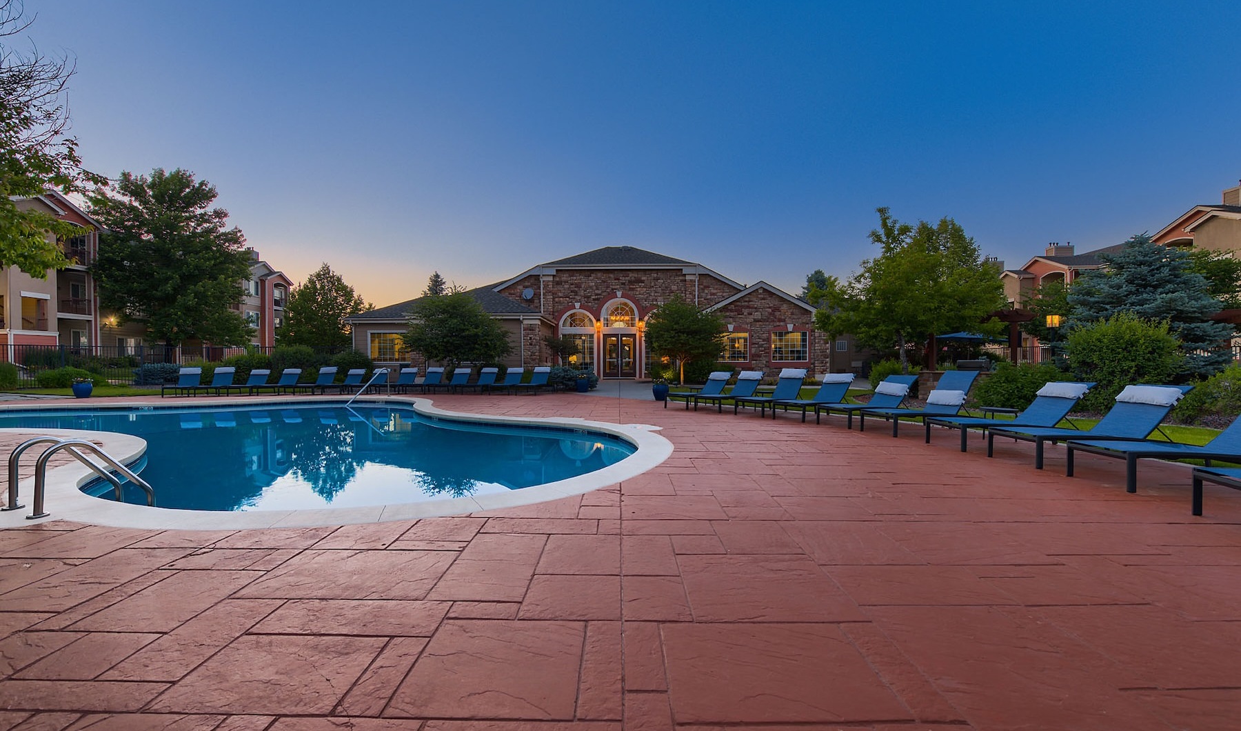 The outdoor pool at Whisper Creek apartments in Lakewood, CO at twilight, surrounded by lounge chairs and trees.