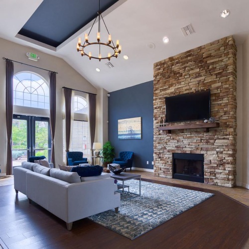 A sofa, coffee table, armchairs, and large mounted TV in the clubroom at Whisper Creek apartments in Lakewood, CO.
